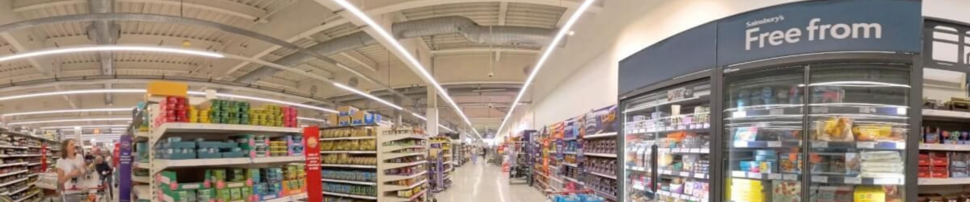 A wide-angle view of a grocery store aisle, featuring a variety of products on both sides. The left shelves hold assorted food items, while the right side displays A wide-angle view of a grocery store aisle, featuring a variety of products on both sides. The left shelves hold assorted food items, while the right side displays